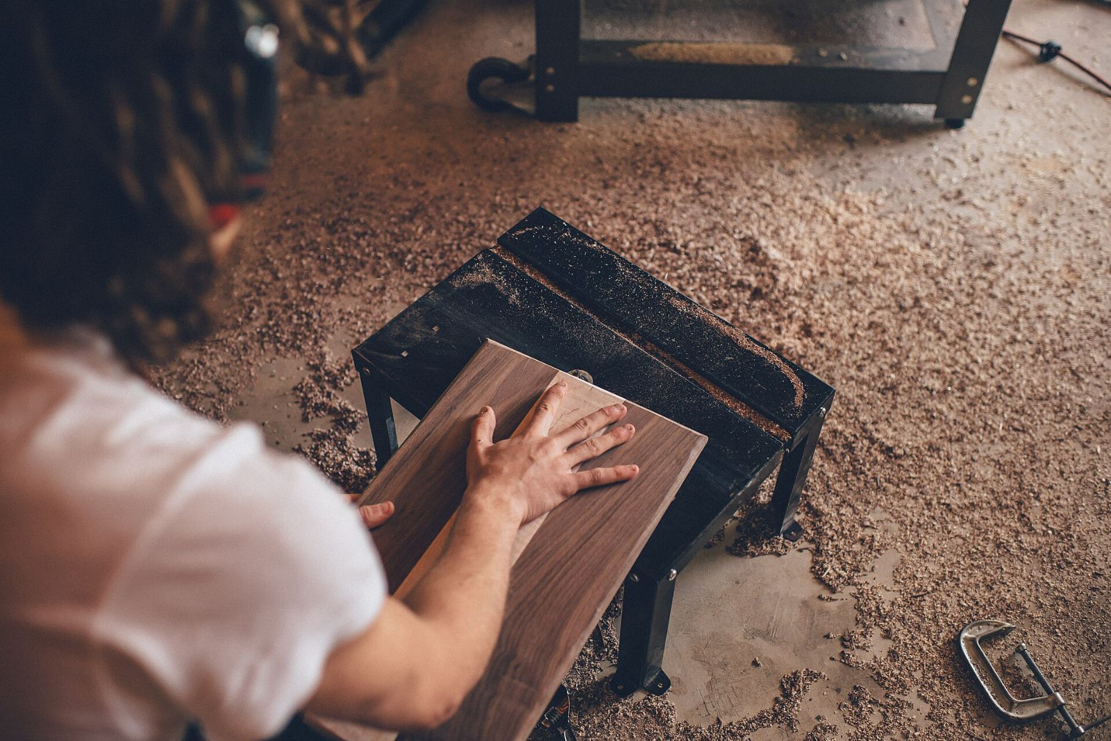 A woodworker's hands smoothing a dark wooden board on a workbench